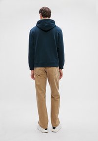 Felpa con cappuccio blu navy e vestibilità comoda, abbinata a pantaloni chiari color khaki. Presenta una tasca a marsupio e polsini a coste.