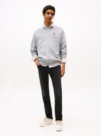 Grijze sweatshirt met logo, gelaagd over een roze en wit gestreept shirt. Gecombineerd met zwarte jeans en witte sneakers. Lange mouwen, casual pasvorm.