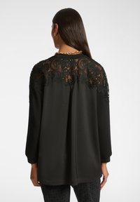 Blusa negra con intrincados detalles de encaje en la espalda, mangas largas y un ajuste holgado. Tejido suave con una textura delicada.
