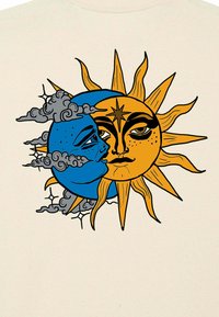 Un tissu de couleur crème présente une lune bleue avec un visage et un soleil jaune avec des rayons, entourés de nuages gris et d'une étoile centrale en accent.