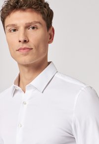 Camicia bianca con collo classico, realizzata in tessuto morbido. Presenta bottoni in perla e un design slim fit.