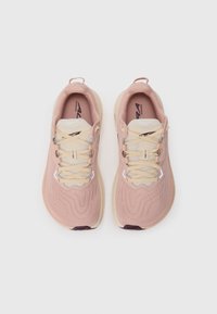 Baskets de course rose clair avec une tige texturée, lacets crème et un design de semelle distinctif. Logo de la marque présent sur la semelle intérieure.