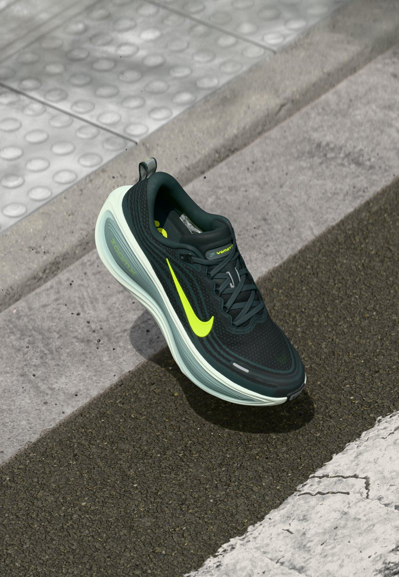 Črne in neonsko zelene Nike tekaške čevlje z ZoomX podplatom, ki lebdi blizu robnika in taktilne površine.