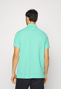 Turkos polo skjorta med krage, korta ärmar och rak nederkant. Tillverkad av ett mjukt, slätt tyg och har en enkel design.
