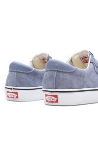 Baskets en daim bleu avec semelles blanches, logo rouge signature sur le talon et détails de surpiqûres contrastantes. Bout arrondi et design bas.