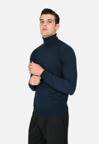 Maglione a collo alto blu navy in morbido tessuto, con maniche lunghe e un design aderente, abbinato a pantaloni neri su misura.