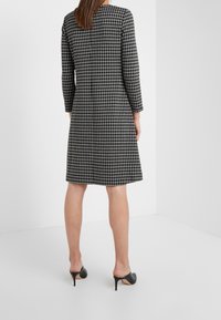 Černobílé kostkované šaty s dlouhými rukávy a kulatým výstřihem, s těsným korzetem a rozšířenou sukní, doplněné černými podpatky.