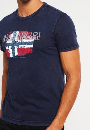 Man wearing a navy blue Napapijri t-shirt with a distressed Norwegian flag design on the chest.