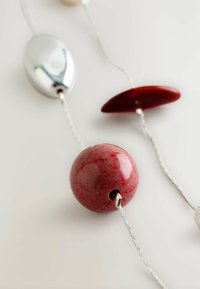 Närmast av ett halsband med stora röda och silverfärgade pärlor på en tunn silverkedja mot en vit bakgrund.