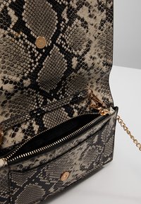 Sac à main imprimé serpent en beige et noir, avec un design structuré, quincaillerie dorée et un compartiment zippé avec une bandoulière en chaîne.
