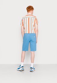 Kortermet, stripete skjorte med oransje, blå og hvite striper; sammen med blå shorts med baklomme; hvite sokker og blå joggesko.