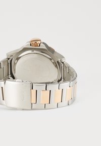 Montre en acier inoxydable avec un accent en or rose, featuring une lunette texturée et un bracelet en métal brossé avec des maillons polis alternés.