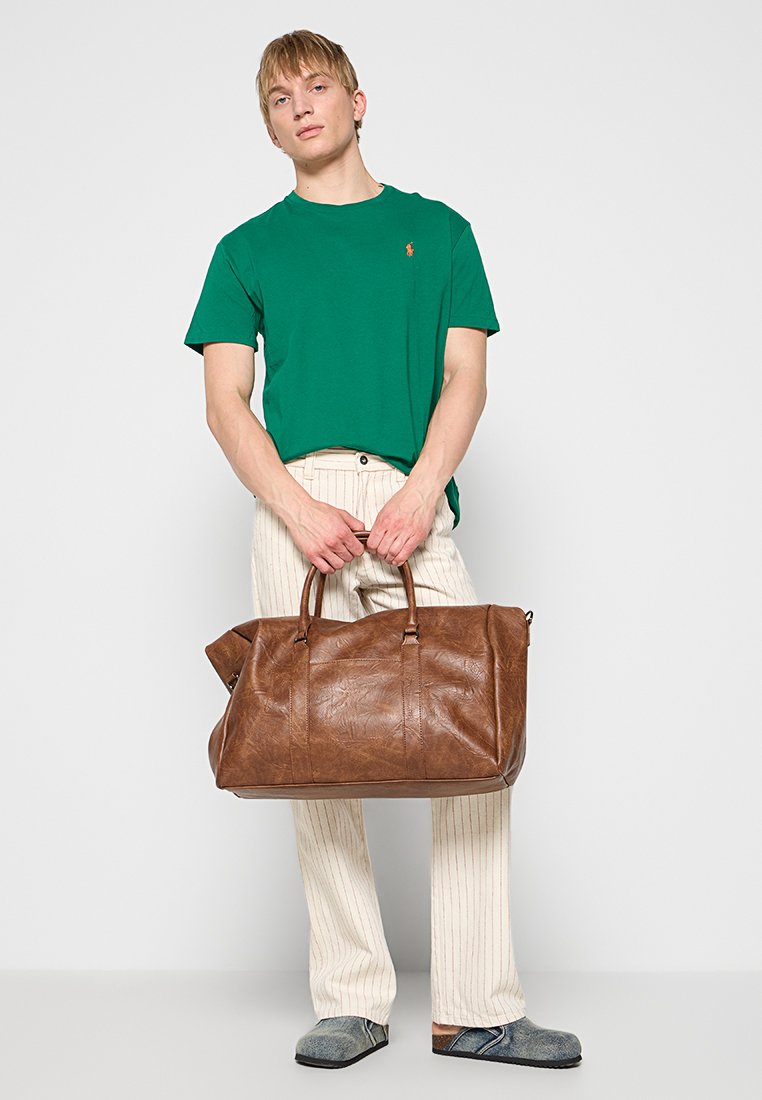 Brązowa skórzana torba podróżna z dwoma uchwytami i zapięciem na zamek, charakteryzująca się teksturowaną powierzchnią i przestronnym wnętrzem, idealna do podróży lub przechowywania.
