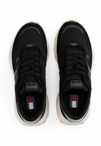 Zapatillas negras que presentan una combinación de materiales de ante y textil, puntera redonda, cordones planos y suela de color crema con un patrón texturizado.