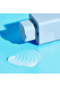 Light blue plastic bottle with a square cap, dispensing a transparent gel forming a wavy pattern on a matching blue surface.