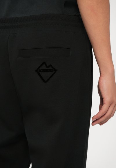 Sorte joggerbukser med elastisk talje, baglomme og et tekstureret logo formet som et bjerg på højre bag.