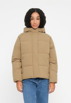 Hnědá prošívaná bunda s kapucí, která má prošívaný design, přední zip a dvě boční kapsy. Nositá přes modré džíny.