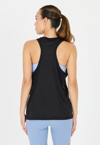 Musta urheilullinen tanktoppi, jossa on urheilullinen takaosa ja kevyt rakenne. Puettu vaaleansineän paidan päälle, mikä luo kerroksellista ilmettä.