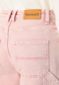 Roza kavbojke iz jeansa z usnjeno oznako Timberland na hrbtni strani. Imajo dve zadnji žep in kontrastne šive na šivih.
