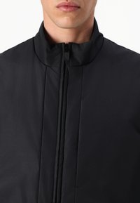 Svart, glidelåsjakke med høy krage og glatt tekstur. Minimalistisk design uten synlige mønstre eller aksenter.