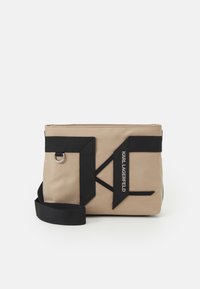 Borsa in nylon beige con accenti in tessuto nero e logo 'Karl Lagerfeld'. Presenta una chiusura con zip e una tracolla rimovibile. Forma rettangolare.