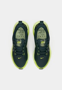 Mørkgrønne joggesko med gule detaljer, mesh-overdel, polstret krage og snøringslås. Har Nike-logo og trykt innerskilt.