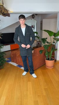 Manteau long gris à carreaux avec col, boutonné, porté par-dessus un t-shirt blanc. Jean bleu et baskets blanches complètent la tenue. Cadre intérieur.