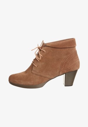 Stivale alla caviglia in suede marrone con punta rotonda, lacci anteriori, colletto corto, tacco impilato e dettaglio di cucitura laterale per una maggiore texture.