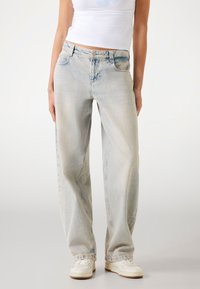 Ljusblå, löst sittande jeans gjorda av denim. Har fem fickor och knäppning med knapp. Slät textur med blekta områden på tyget.