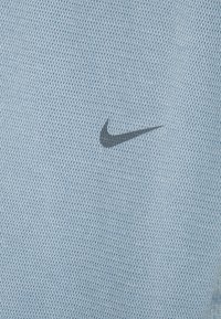 Hellblaues Nike T-Shirt aus strukturiertem Stoff mit einem dunkelgrauen Swoosh-Logo, das auf der Vorderseite gestickt ist.