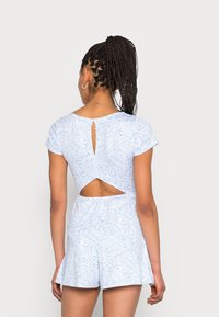 Blå jumpsuit med paisleymönster, korta ärmar, nyckelhålsdetalj på ryggen och utskärningsaccent. Mjuk tyg, avslappnad passform, utställda shorts.