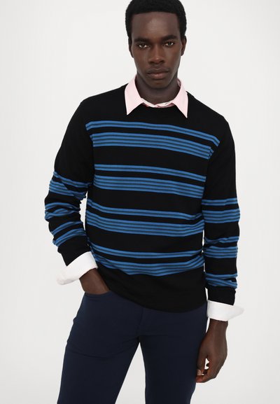 Pull noir avec des rayures horizontales bleues, superposé à une chemise collier rose clair. Mettre l'accent sur la coupe ajustée et le matériau en tricot texturé.