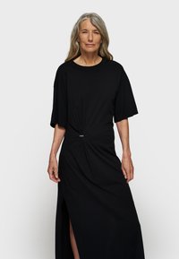 Czarna sukienka z miękkiego materiału, z krótkimi rękawami, z detalem w postaci węzła w pasie oraz bocznym rozcięciem, które zapewnia swobodę ruchów.
