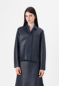 Navy leather cropped jacket with a button-up front, pointed collar, and single chest pocket; paired with a matching leather skirt.