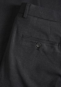 Pantalon formel gris foncé avec une poche arrière comportant un seul bouton noir et des passants de ceinture.