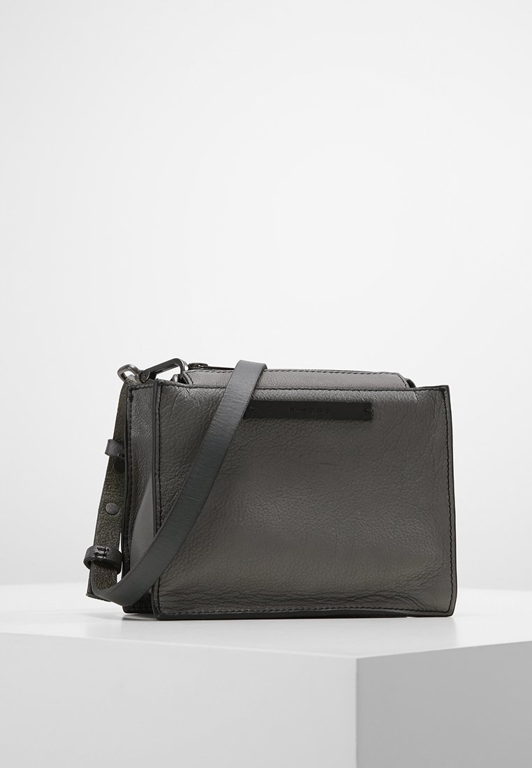 Bolso bandolera de cuero gris con forma estructurada, correa ajustable y sutiles detalles metálicos. El acabado texturizado añade profundidad.