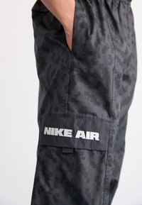 Cargo bukser i mørkegrå med pixelmønster, elastisk talje, sidelommer og "NIKE AIR" logo i hvid på benet.