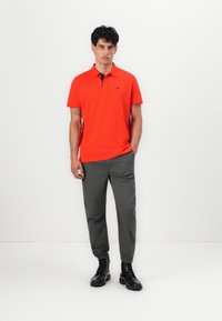 Lys orange polo-skjorte med krage, kombinert med grå pressede bukser. Antrekket fullføres med svarte snøreb Boots.