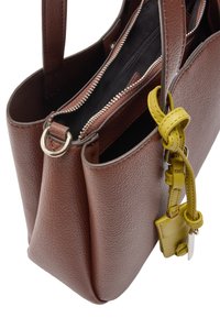 Brązowa skórzana torba tote z fakturą w łuski, podwójnymi przegrodami zapinanymi na zamek oraz jasnoskalnym żółtym paskiem przyczepionym do małej metki.