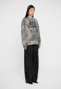Sweatshirt oversized, em tie-dye cinza com letras pretas. Combinado com calças largas pretas e sapatos de bico fino. Textura de tecido suave.