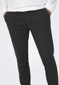 Pantalons gris foncé en tissu doux, présentant un design fuselé avec des poches latérales et des détails de couture discrets.