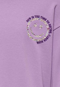 Lavendel sweatshirt met een smiley-gezichtsontwerp omlijnd met kleurrijke bloemmotieven, met de tekst "NU IS HET DE TIJD OM TE BESLISSEN, ZORG."