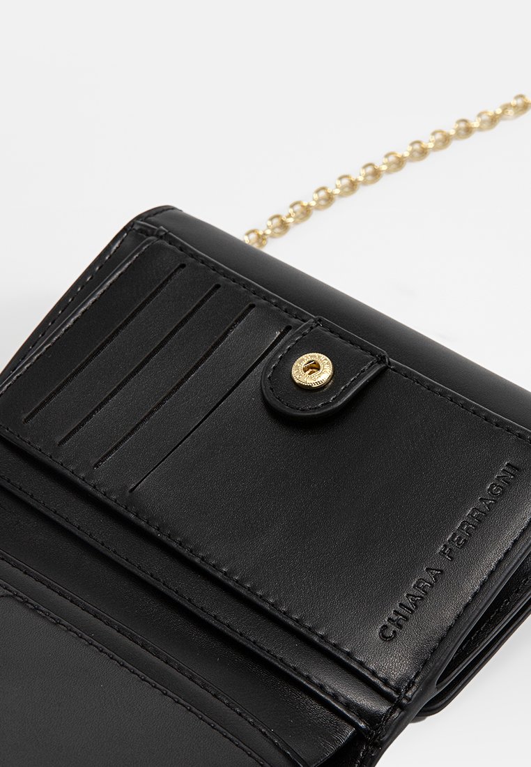 Cartera de cuero negra con herrajes dorados, que cuenta con ranuras para tarjetas y un cierre de presión. Incluye una cadena dorada para llevarla. Textura suave.