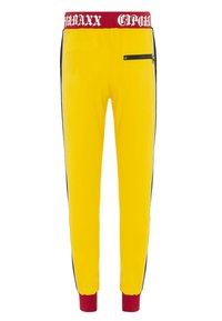 Gelbe Jogginghose mit einem roten Logo-Bündchen, schwarzen Seitenstreifen und einer Reißverschlusstasche auf der Vorderseite. Gummizüge an den Knöcheln runden das Design ab.
