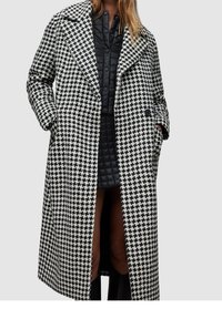 Schwarz-weißes Hahnentrittmantel mit Reverskragen, übergroßer Passform und Seitentaschen, kombiniert mit einer schwarzen gesteppte Innenjacke.