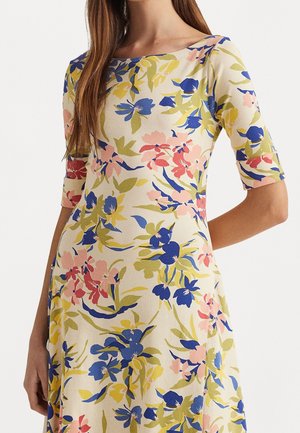 Robe fleurie en tissu crème ; présente des fleurs bleues, roses et vertes ; décolleté bateau et manches à la longueur du coude ; forme évasée fluide.
