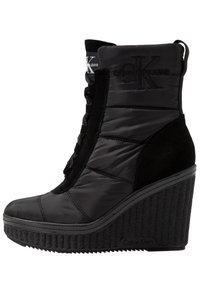 Černé wedge boty s kombinací prošívaného syntetického svršku a semišových akcentů. Výrazný logo detail na límci a texturovaná podrážka.