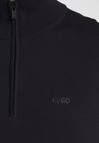 Marinblå zip-up tröja i ribbat stickat tyg, med hög krage och subtil "HUGO" brodyr i matchande färg.