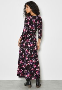 Vestido largo negro con estampado de flores en tonos rosa y púrpura, mangas largas, cintura ajustada y falda fluida. Combinado con botas negras.