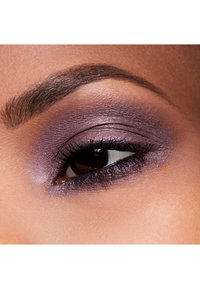 Gros plan sur un œil richement coloré avec un fard à paupières métallique violet, un eyeliner noir épais et des sourcils bien définis et soignés sur une peau lisse.
